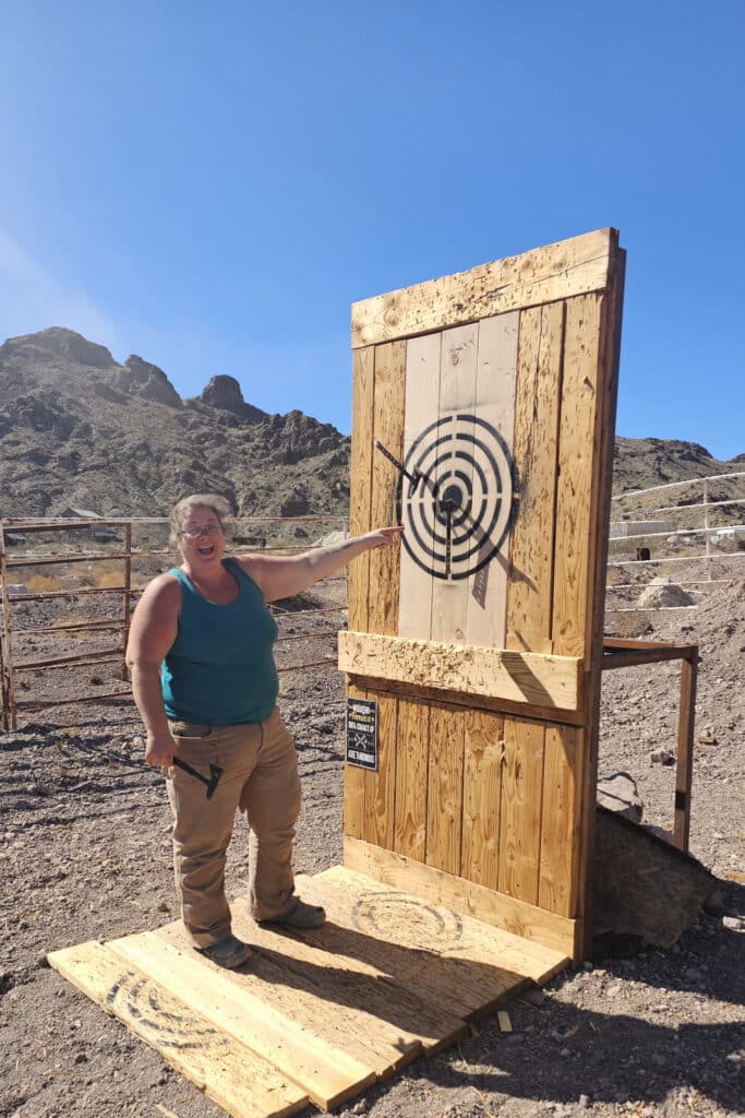 Smiling woman in Eldorado Canyon near Las Vegas, pointing at axe target after a fun Nevada ghost town sightseeing adventure.