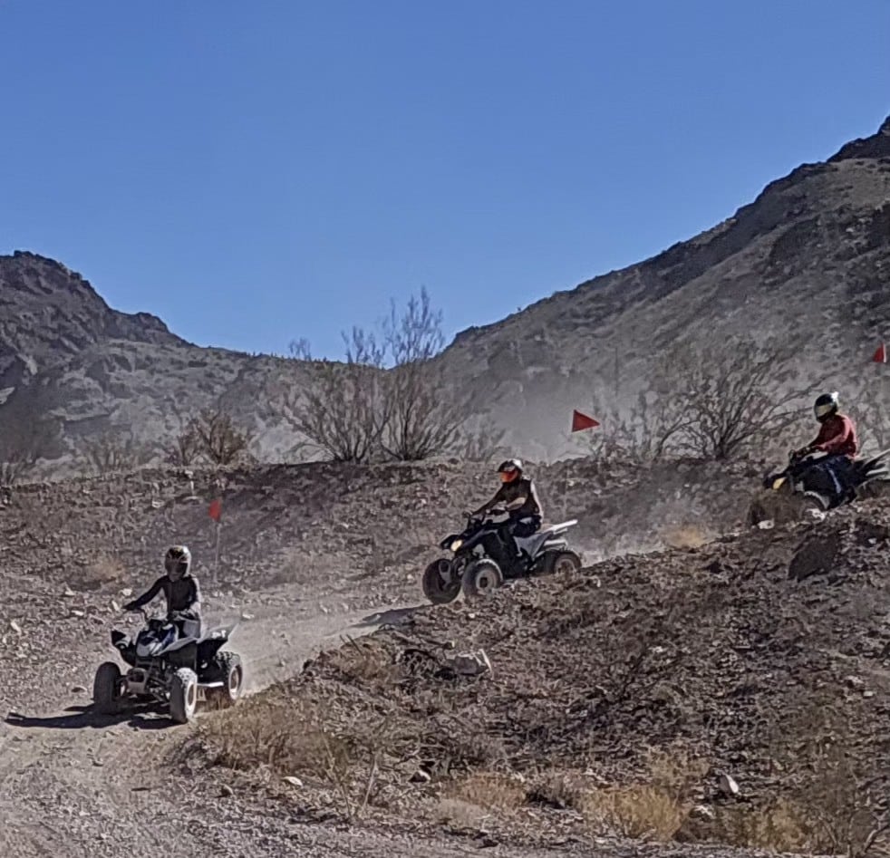 Riders enjoy a Las Vegas ATV tour near rocky Nevada hills, red flags flying under blue skies along the desert trail.