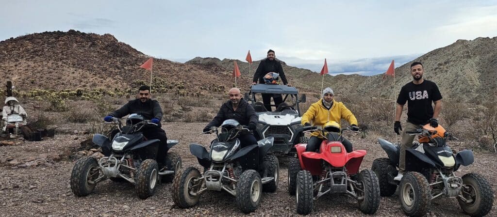 Group enjoys an exciting Las Vegas ATV tour in Nevada desert with ATVs, RZR, red flags, and mountains near the Colorado River.