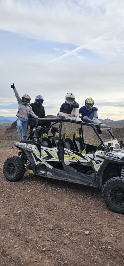 Group on Polaris RZR during Las Vegas ATV tour near Nevada mountains, posing for adventure with helmets amid rocky terrain.