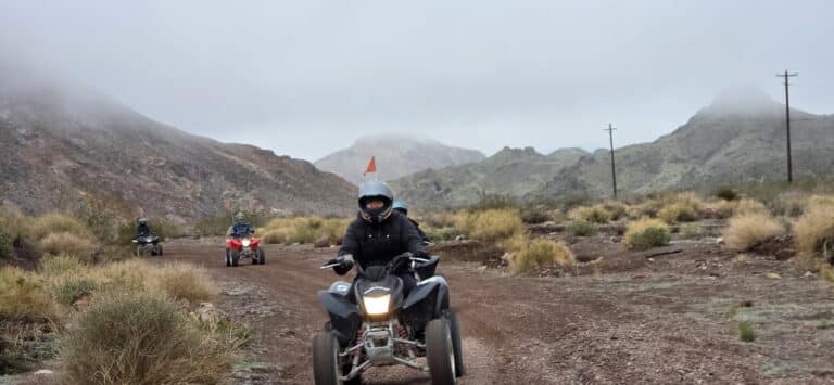 ATV riders explore a rocky Nevada trail near Las Vegas, with mountains, sparse bushes, and cloudy skies on an exciting off-road tour.