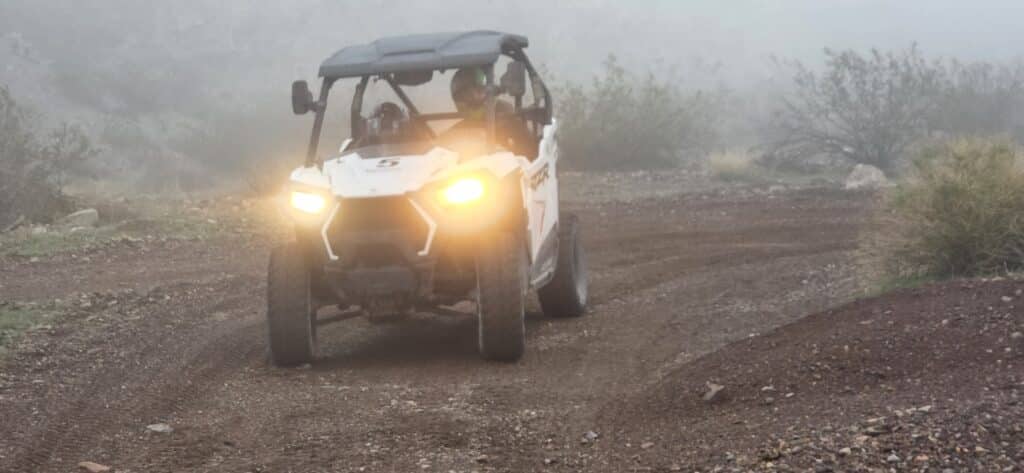 RZR off-road vehicle with headlights on drives a rugged, misty Nevada trail near Las Vegas—perfect for ATV tours and adventure.
