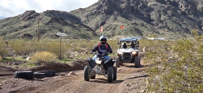 Riders in helmets explore a Nevada desert trail near rocky mountains on an ATV and RZR, perfect for Las Vegas off-road tours.