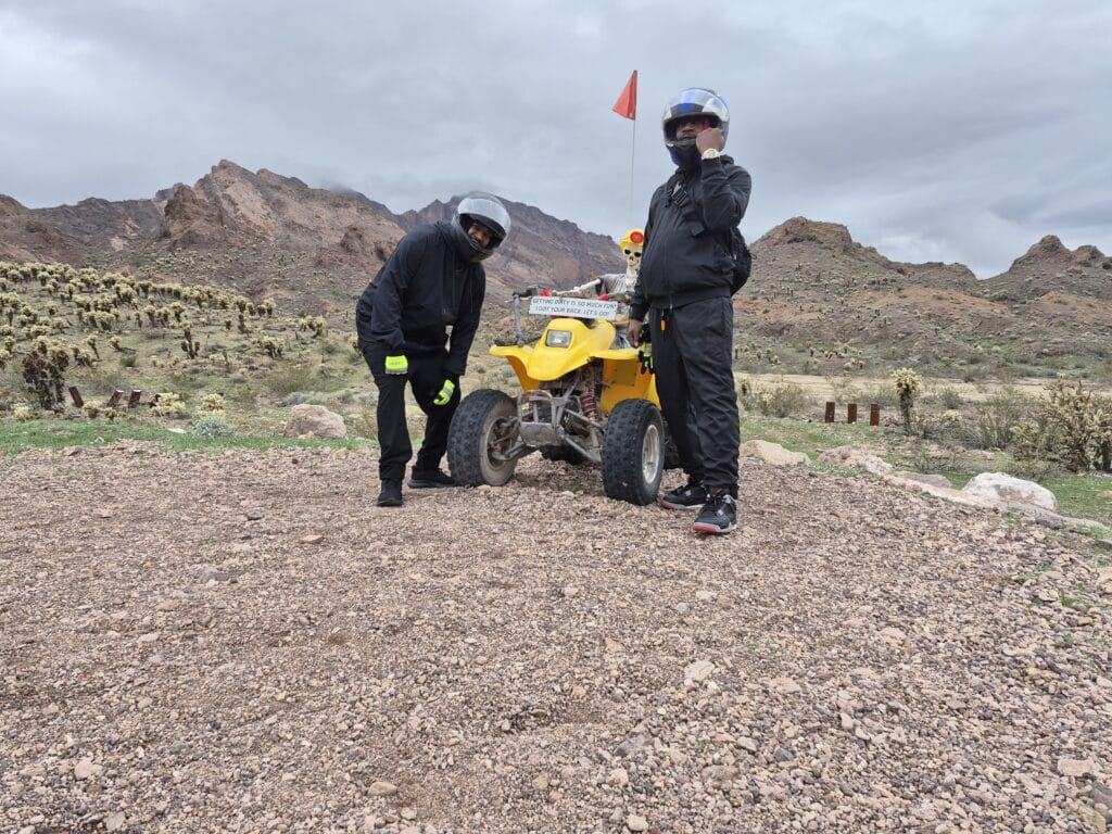 Adventurers in helmets stand by a yellow ATV on a Nevada trail near cacti and mountains—Las Vegas ATV tours excitement.