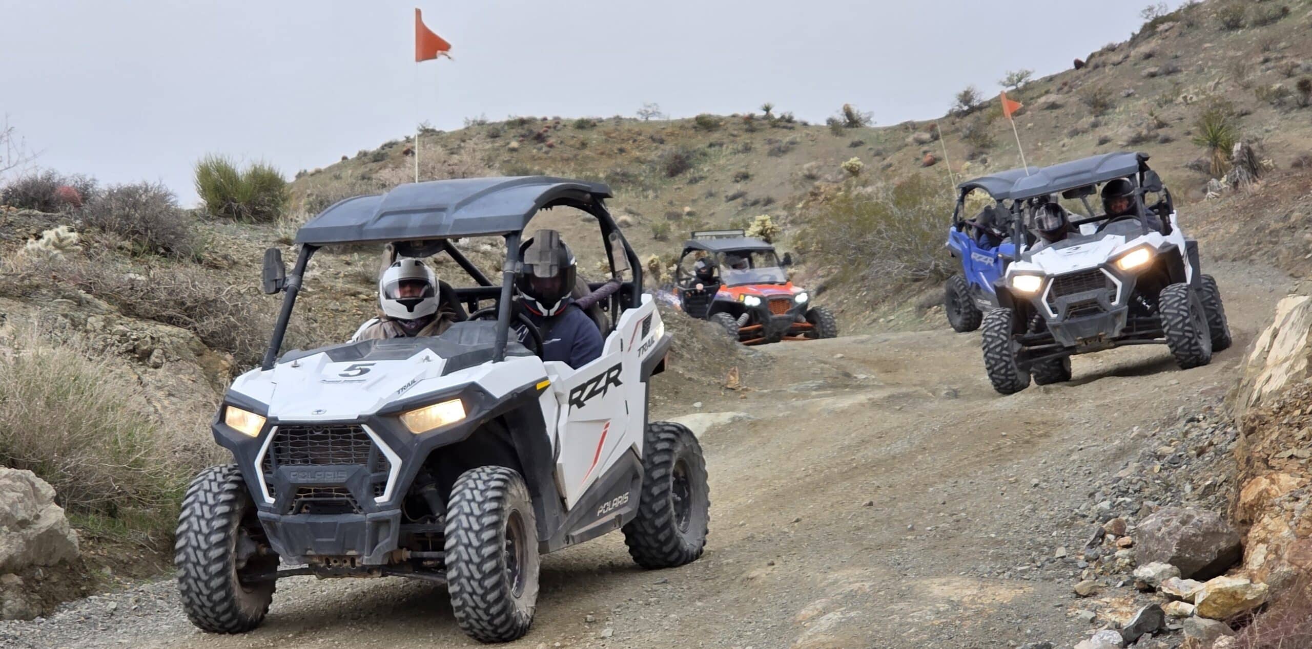 ATVs with flags drive a rocky desert trail near Las Vegas on an RZR tour to the Colorado River and Nevada ghost towns.