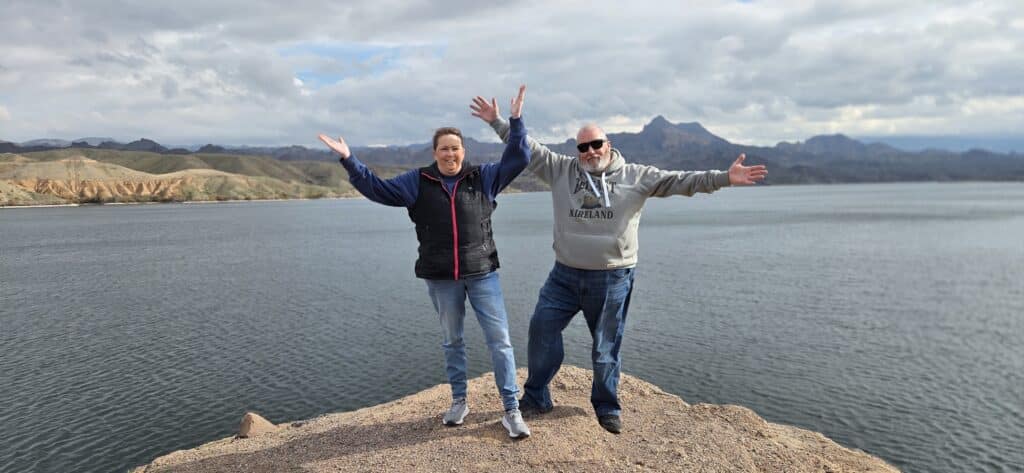 Two people on a rocky edge by the Colorado River near Las Vegas, Nevada, smiling and raising arms after ATV tour adventure.