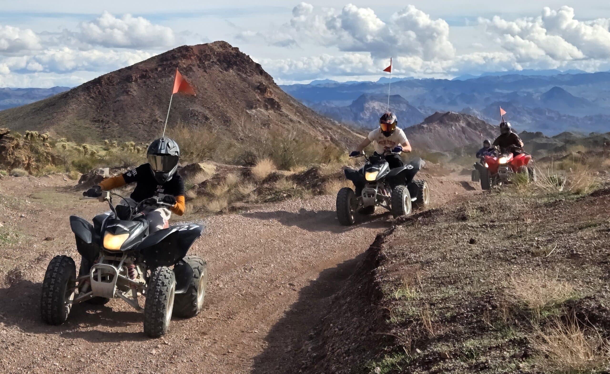 ATV riders explore a rugged Nevada trail near Las Vegas, with orange flags waving by rocky hills—perfect for thrilling ATV tours.