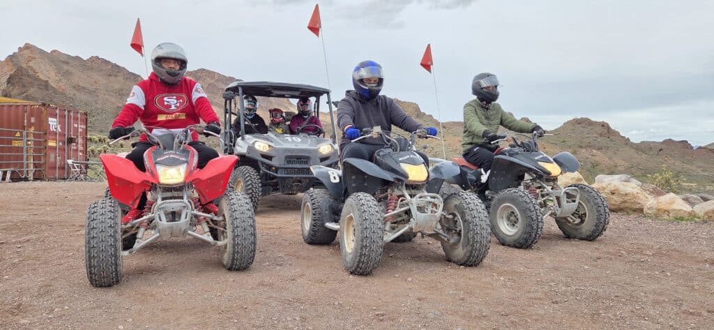 Adventurers on ATVs and a UTV ride a rocky Nevada trail near Las Vegas, red flags flying, perfect for ATV tours or RZR off-road fun.