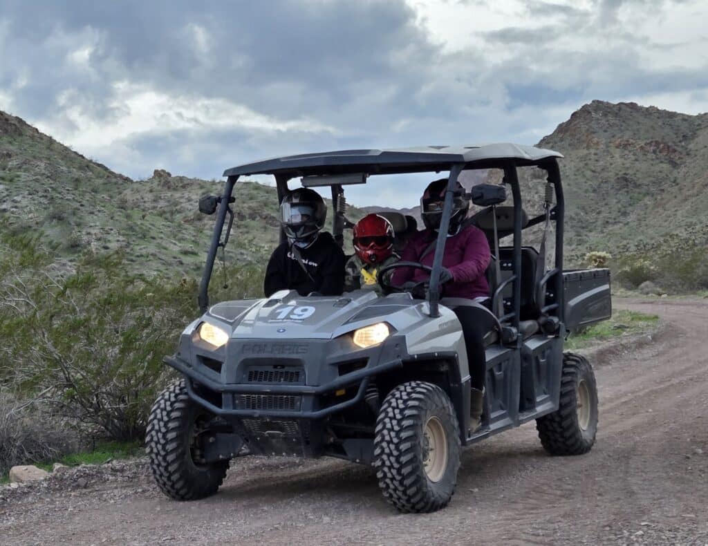 Group in helmets and jackets rides ATV on Las Vegas desert tour near Eldorado Canyon, Nevada, exploring rocky terrain under cloudy skies.