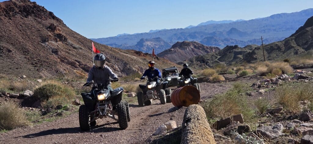 Adventurers ride ATVs in Nevada desert near Las Vegas, navigating rocky trails, logs, and barrels on an exciting off-road tour.