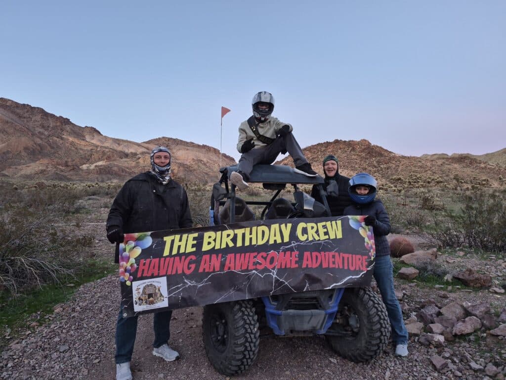 Four friends in helmets pose by an RZR off-road vehicle near Las Vegas, Nevada desert—Birthday Crew ATV adventure!.