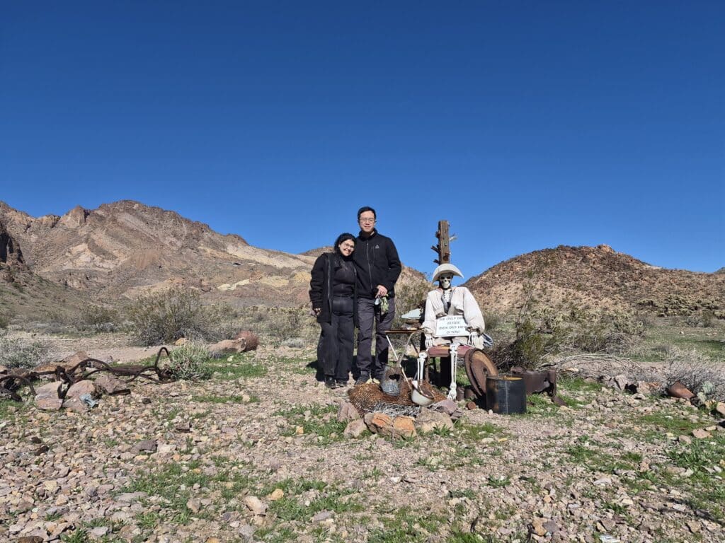 Smiling friends in black coats beside a mannequin in white, enjoying Nevada desert near Las Vegas and the Colorado River.
