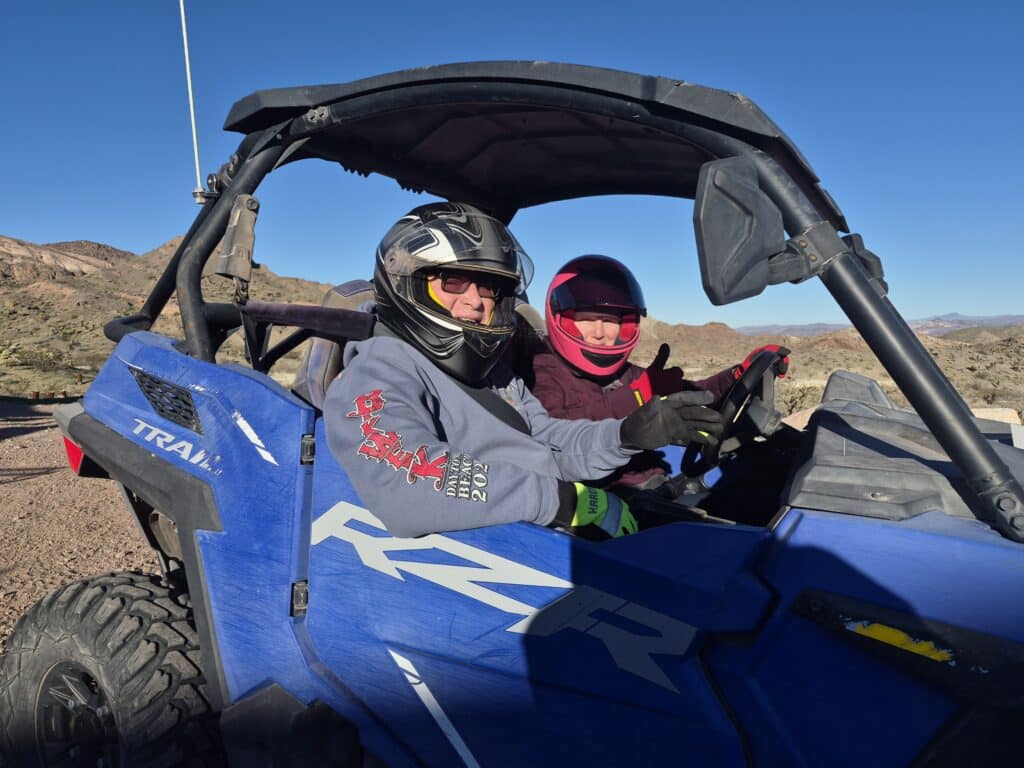 Two riders in helmets enjoy a RZR off-road ATV tour near Las Vegas, Nevada, with rocky trails and desert mountains in view.