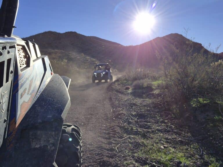 ATV RZR vehicles race along a dusty Nevada trail near Las Vegas, with desert hills and clear skies on an exciting off-road adventure.