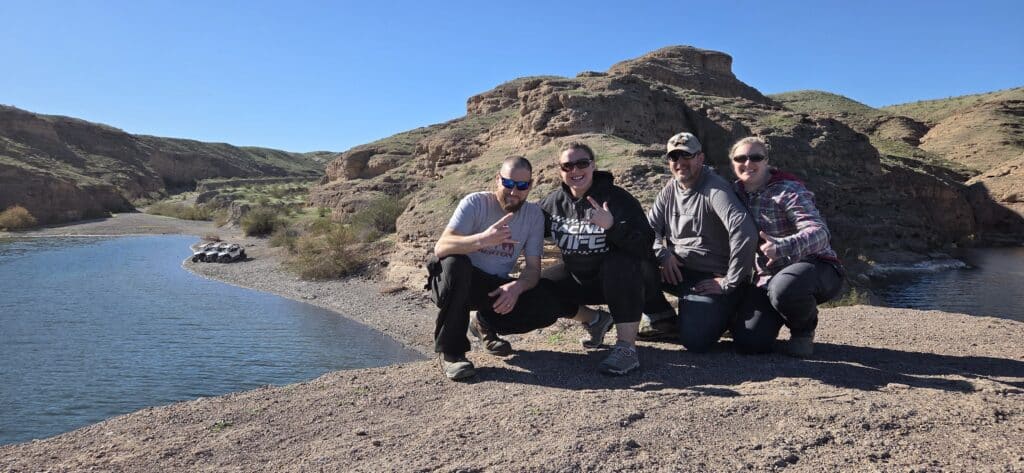 Smiling friends on a rocky Colorado River bank in Nevada during a Las Vegas RZR off-road ATV tour adventure.