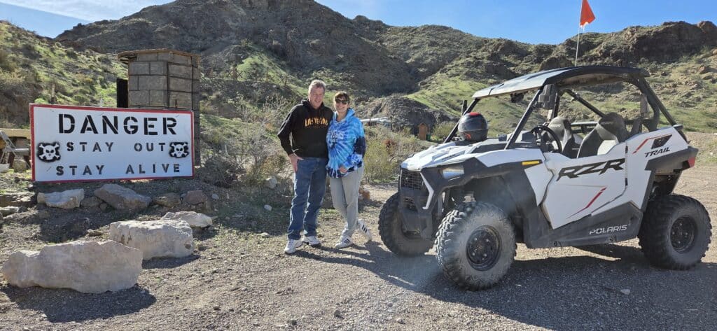 Two people by a white Polaris RZR near a “DANGER” sign amid Nevada’s rocky hills—perfect for Las Vegas ATV or RZR off-road tours.