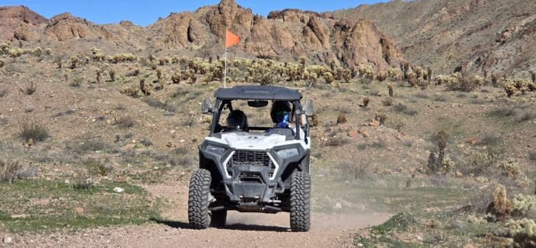Las Vegas ATV tour: White off-road vehicle on rocky desert trail near cacti and hills under clear blue Nevada sky, Colorado River nearby.
