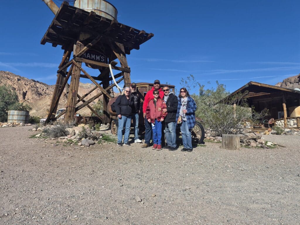 Group at a rustic HAMMS water tower in Nevada Ghost Town near Las Vegas, vintage car and desert plants, perfect for ATV tours.