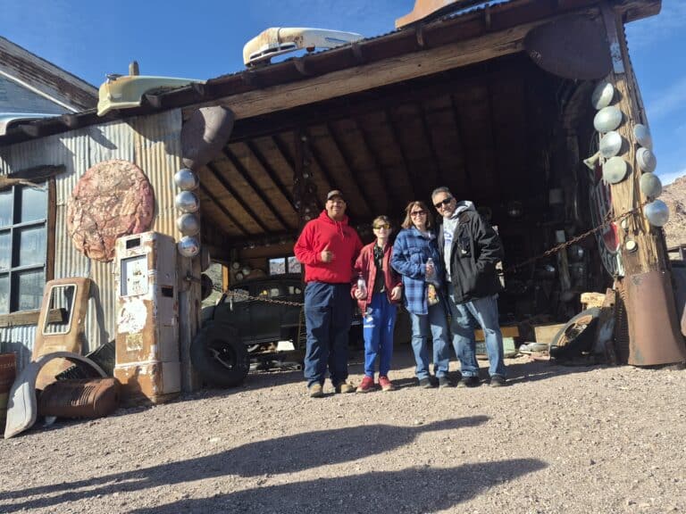 Smiling group at Nevada ghost town garage with vintage cars, perfect for ATV tours near Las Vegas and Colorado River.