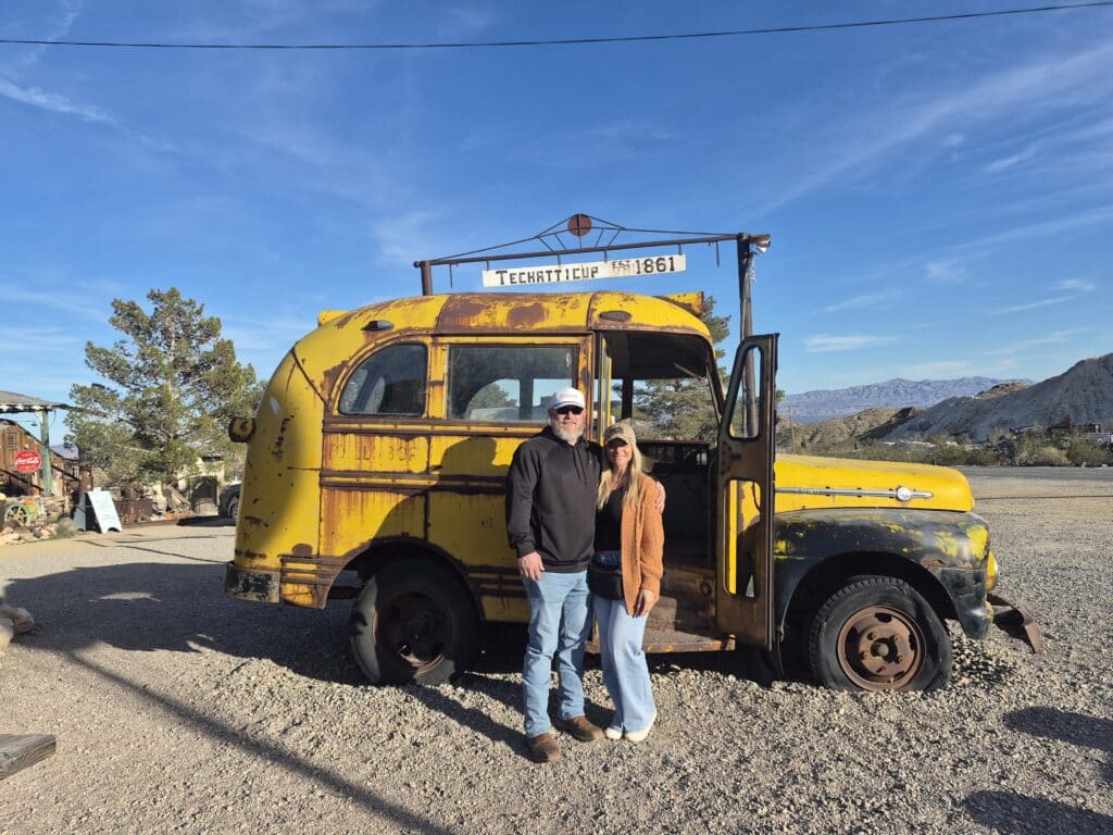 Smiling couple by a rusty school bus in Nevada’s Techatticup Ghost Town near Las Vegas, perfect for ATV and RZR tours.
