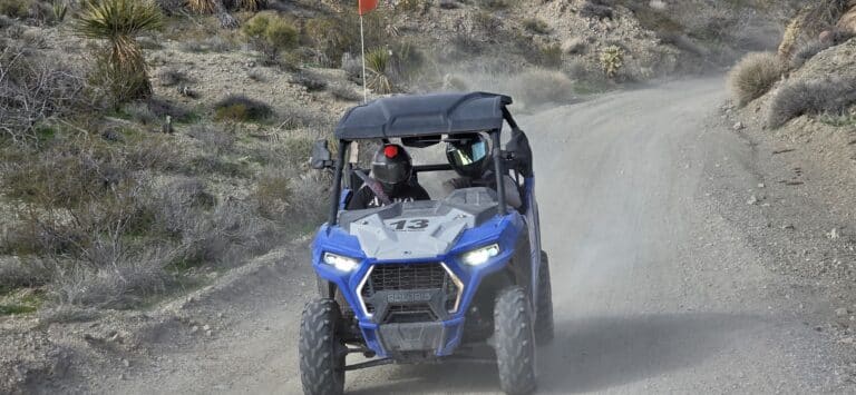 Two riders in helmets drive a blue Polaris RZR #13 on a dusty Nevada desert trail near Las Vegas during an ATV off-road tour.