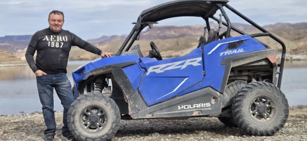 Smiling man in black shirt and jeans by blue RZR on rocky Nevada ground near the Colorado River, perfect for Las Vegas ATV tours.