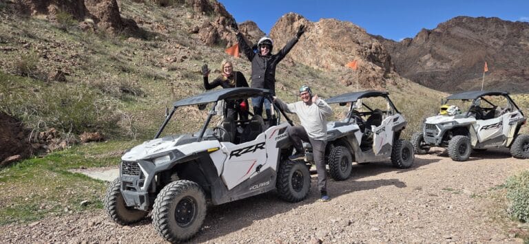 Adventurers pose by white ATVs on a rocky Nevada trail near Las Vegas, with mountains in view—perfect for RZR off-road tours.