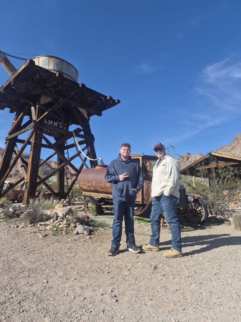 Two people in a Nevada ghost town near Las Vegas stand by a water tower and vintage truck, perfect for ATV tours and sightseeing.