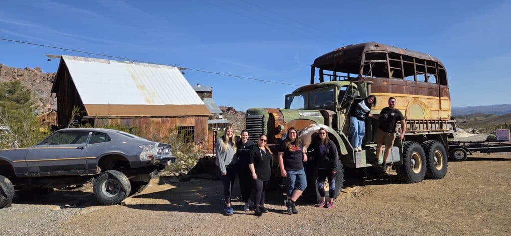 Group enjoying Ghost Town sightseeing near an old truck on an ATV tour in the Nevada desert, close to Las Vegas.