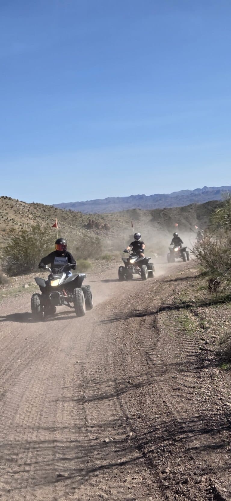 ATV riders on a dusty Nevada desert trail near Las Vegas, with distant mountains—perfect for RZR off-road tours and adventure.