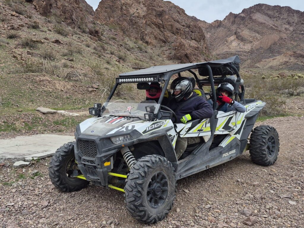 Three riders in helmets and jackets explore a rocky Nevada trail on a Polaris RZR during an exciting Las Vegas ATV tour adventure.