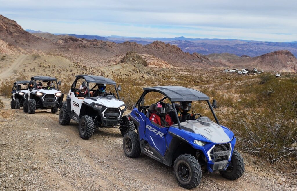 Las Vegas RZR off-road tour: Blue and white ATVs drive desert trails near Nevada mountains, thrilling adventure riders.