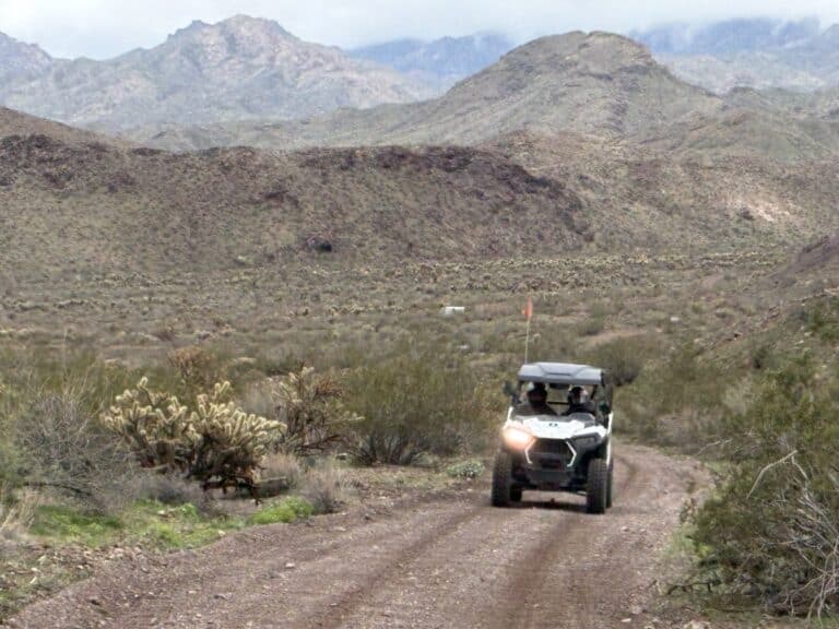 A white off-road vehicle explores a Nevada desert trail near Las Vegas with mountains, perfect for ATV tours or RZR adventures.
