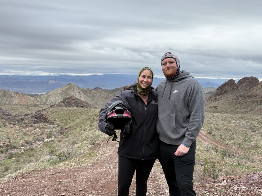 Two adventurers in outdoor gear smile on a rocky Nevada trail near Las Vegas, ready for an ATV tour by the Colorado River.