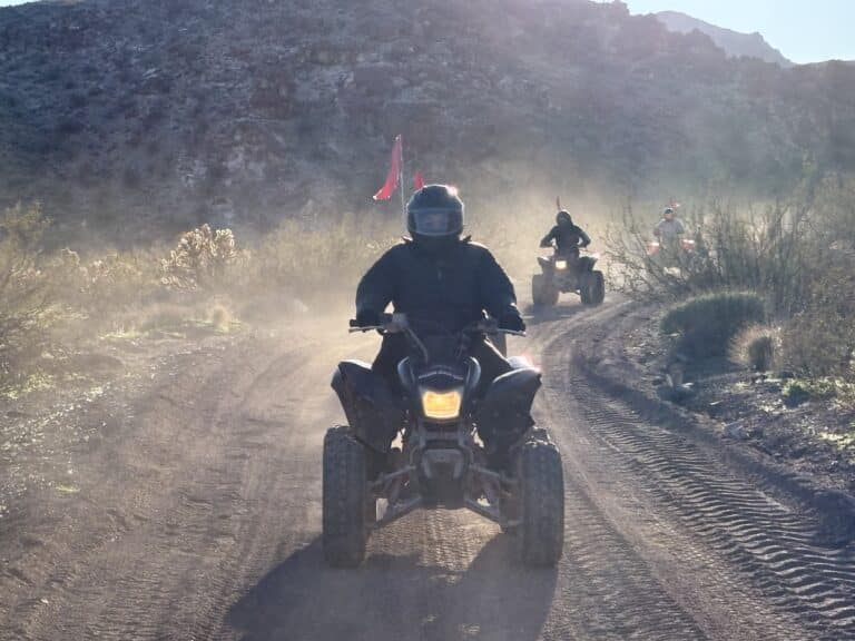 Group rides ATVs on a dusty Nevada trail near Las Vegas, with desert hills and flags—perfect for ATV tours and adventure seekers.
