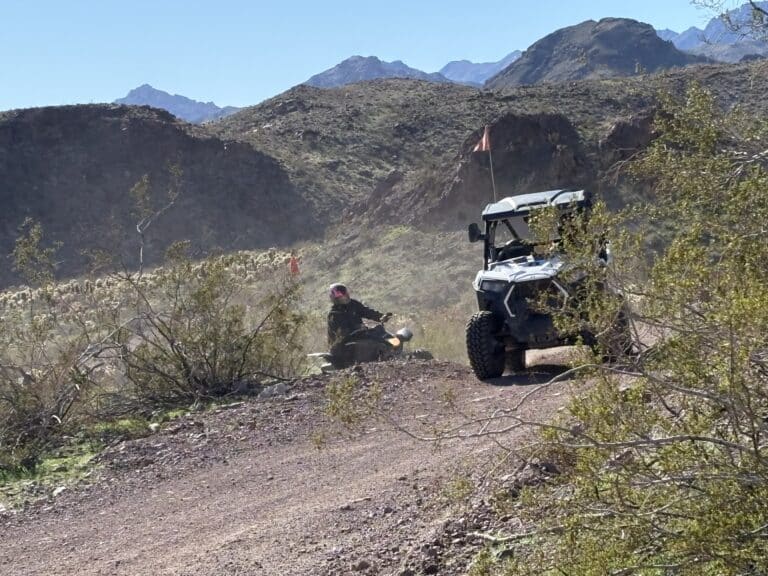 Adventurers on an ATV and RZR explore a dusty Nevada trail near the Colorado River, perfect for Las Vegas off-road tours.