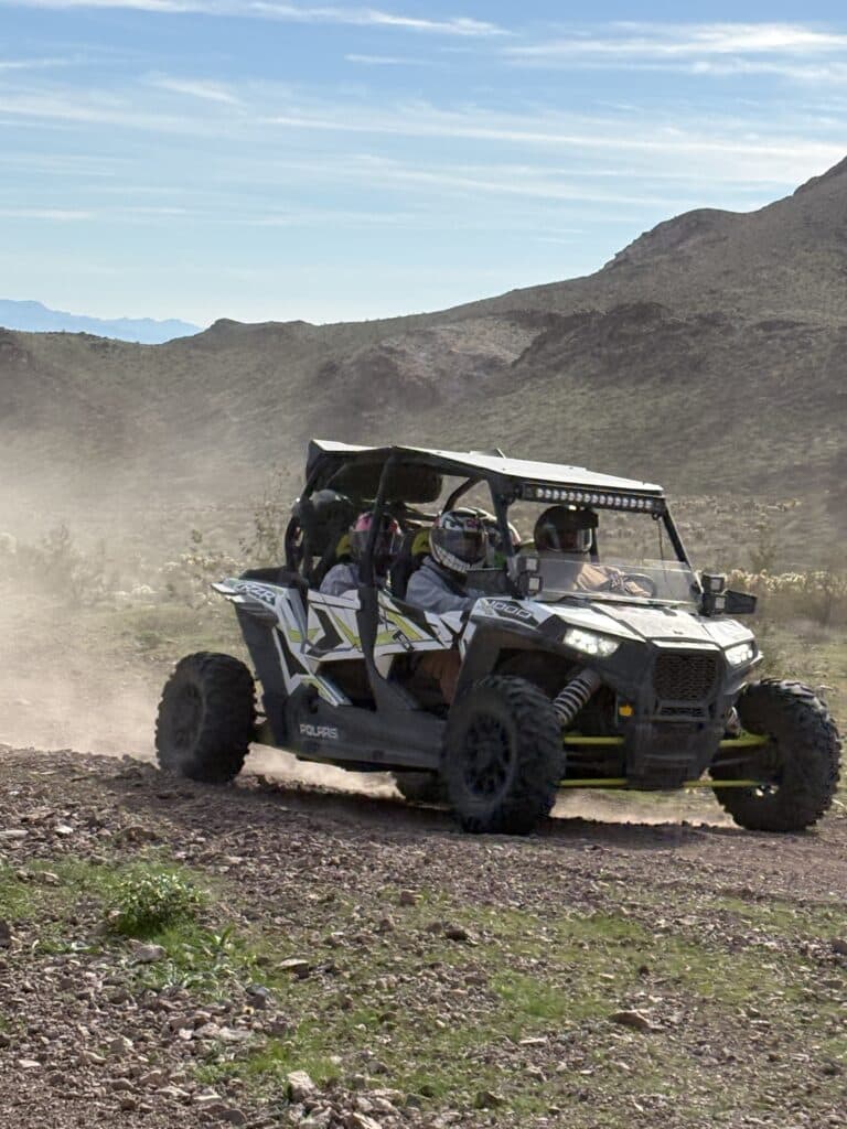 Black and white RZR ATV with two helmeted riders kicks up dust on a desert trail near Las Vegas and the Colorado River, Nevada.
