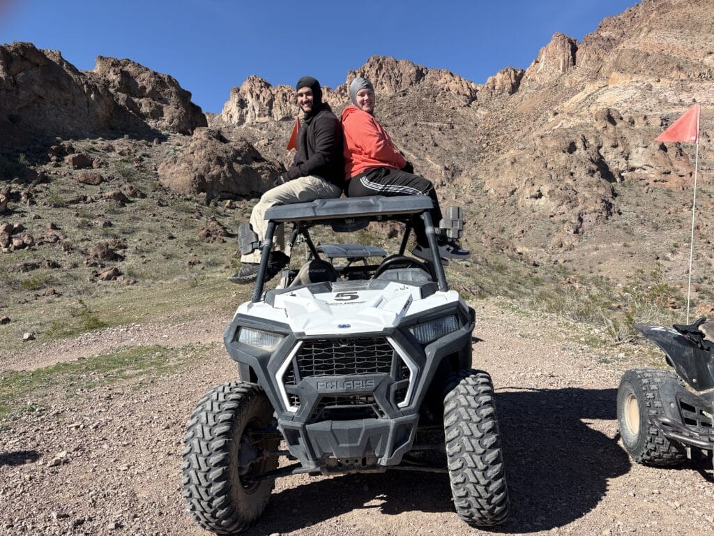 Smiling duo atop a Polaris RZR in Nevada’s rugged hills, clear sky above—perfect for Las Vegas ATV tours and Ghost Town rides.