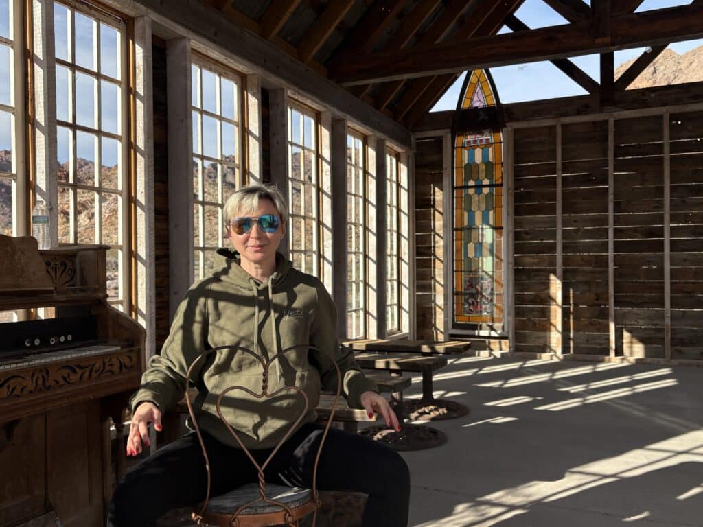 A person in sunglasses and a green hoodie relaxes inside a sunlit Nevada cabin near the Colorado River, perfect for Ghost Town tours.