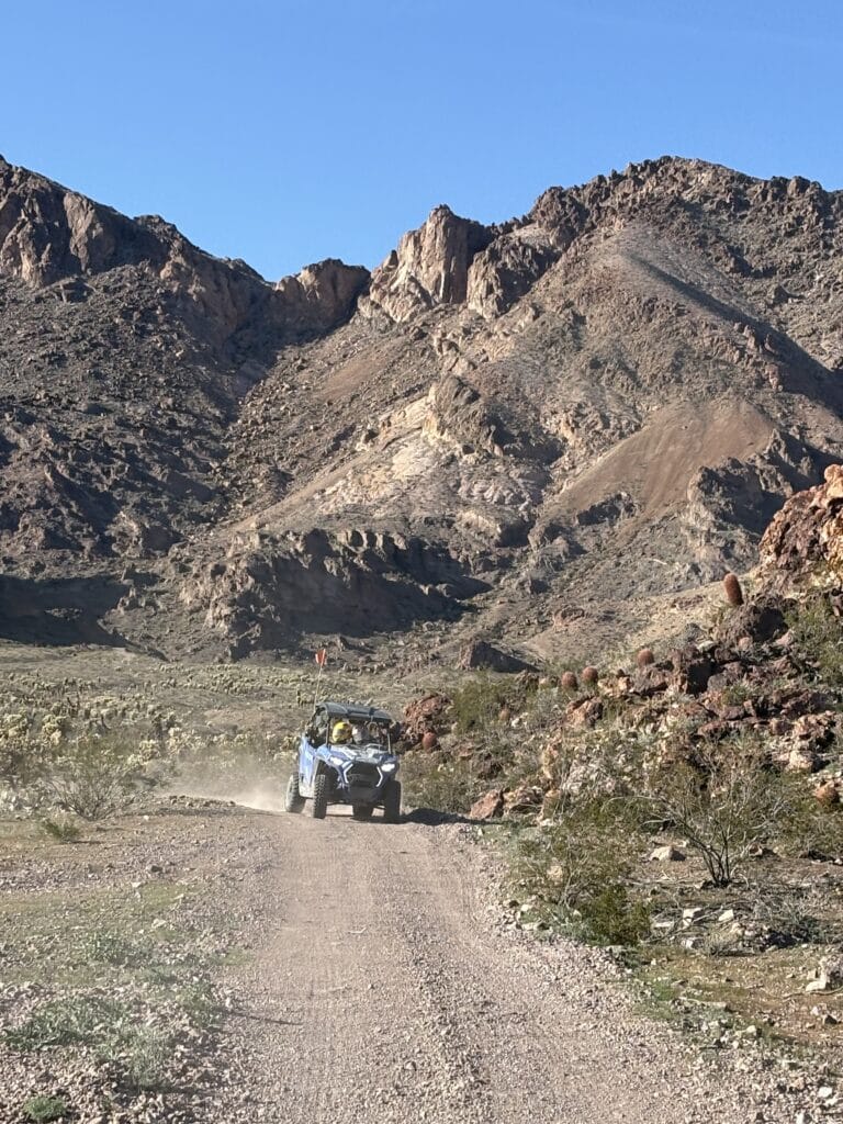 A blue RZR off-road vehicle on a dusty Nevada trail near Las Vegas, rugged desert terrain and mountains under clear skies.