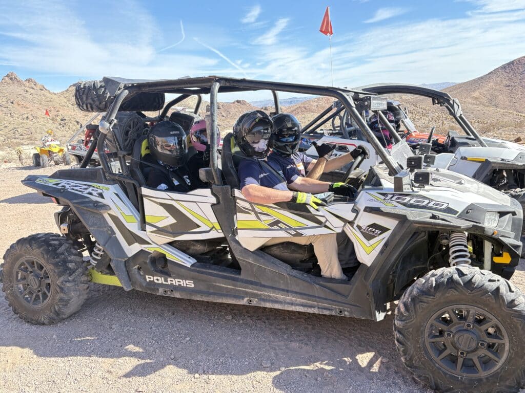 Riders in safety gear enjoy a Polaris RZR off-road tour near Las Vegas, Nevada, with ATVs on desert trails and rocky hills.