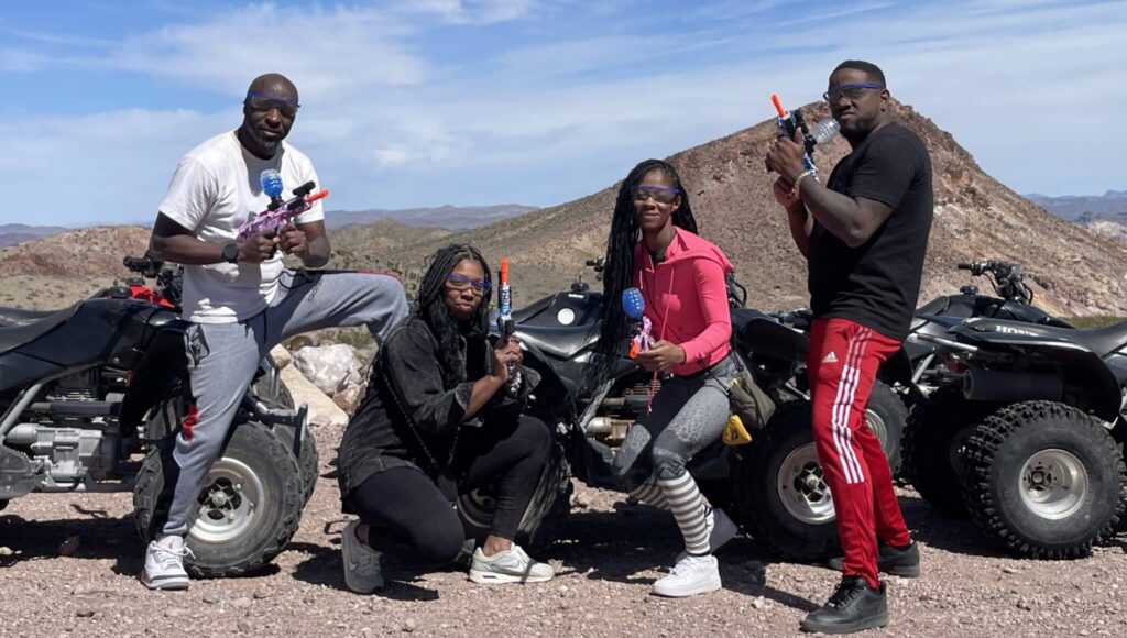 Group enjoying Las Vegas ATV tour in Nevada desert near mountains, posing by ATVs with toy guns and smiles—adventure near Colorado River.