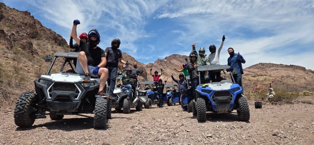 Helmeted group celebrates in off-road vehicles on an Eldorado Canyon ATV tour near Las Vegas, Nevada, with scenic desert views.