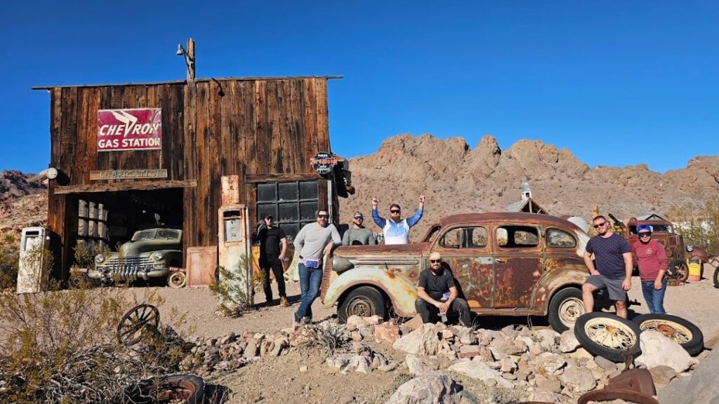 Group by a rusty vintage car at Chevron Gas Station in Eldorado Canyon, Nevada—ideal for Las Vegas ghost town ATV tours.