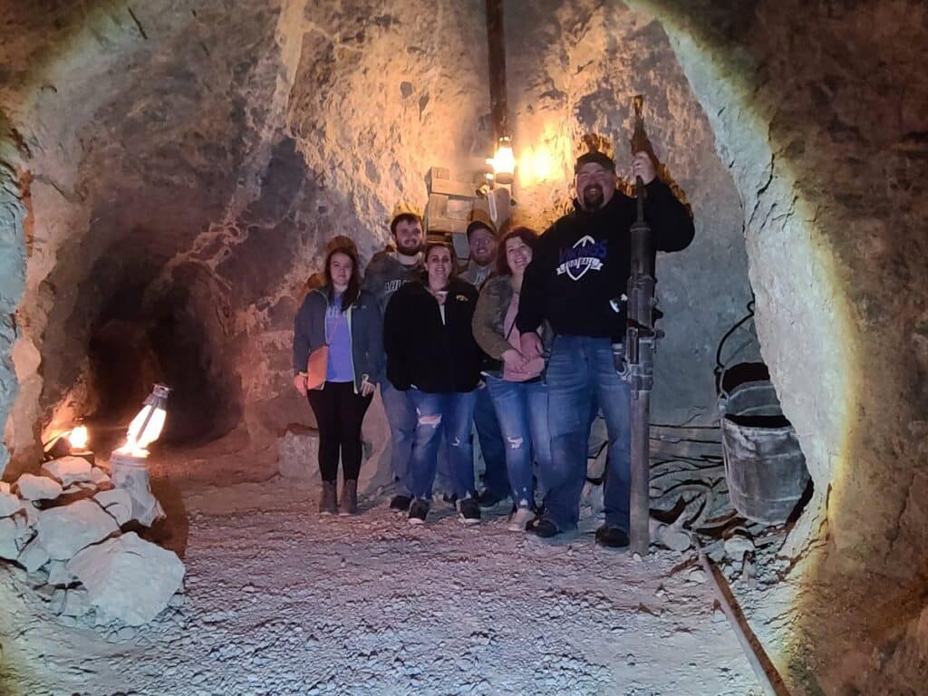 Six on a Las Vegas RZR off-road tour pose in a cave near Nevada’s Colorado River, surrounded by rocks and mining gear.