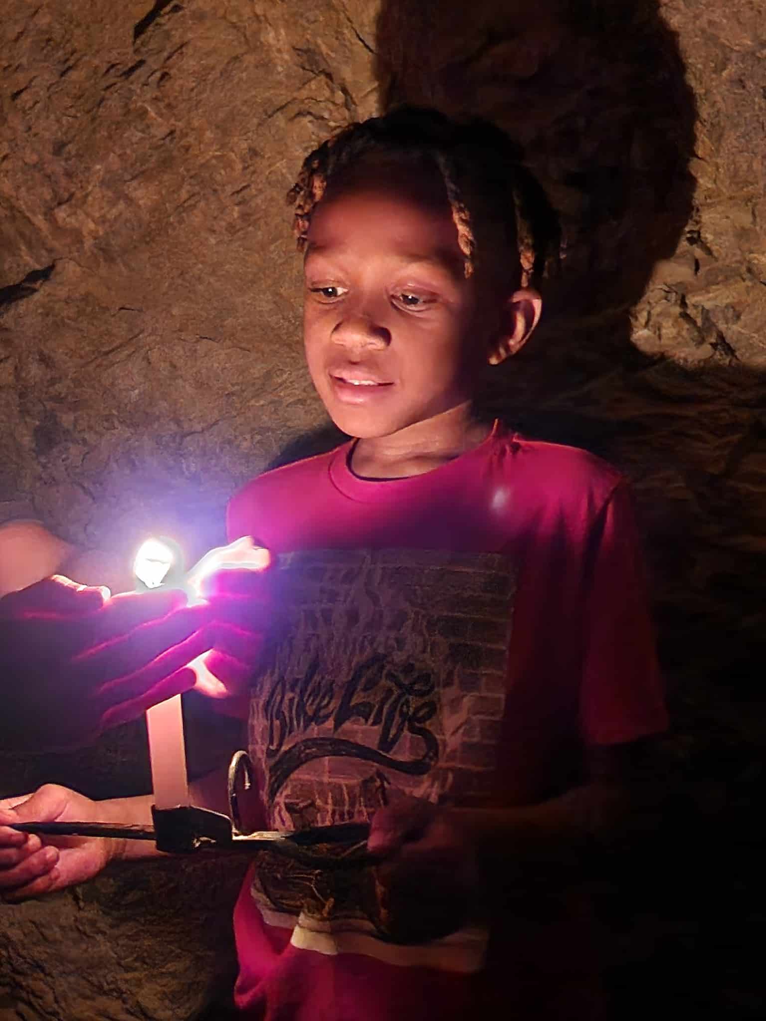 Child in red shirt holding a candle inside Eldorado Canyon near Las Vegas, Nevada—perfect for ghost town sightseeing adventures.
