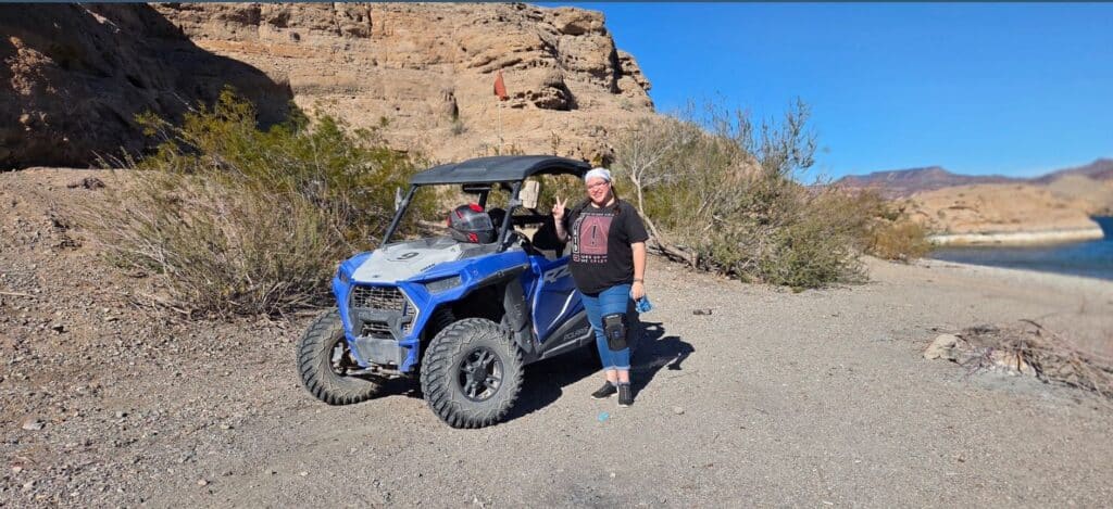 Ayde Cox Manager & Lead Booking Agent Smiling guide by blue ATV in Nevada desert near Las Vegas, Colorado River, with mountains—perfect for RZR off-road adventure tours.