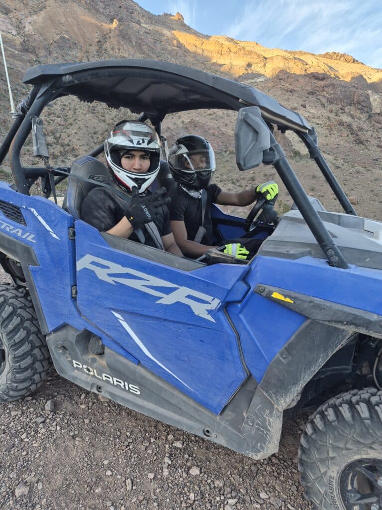 Adventurers in helmets ride a blue Polaris RZR on a rocky Nevada trail near Las Vegas, enjoying an epic ATV tour.
