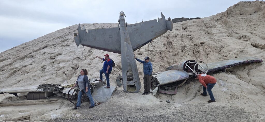 Adventurers explore a rusted plane wreck on Nevada’s rocky hills near Las Vegas during an RZR off-road tour under cloudy skies.