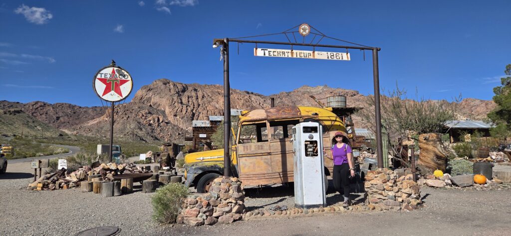 A woman at Techatticup 1861, a Nevada ghost town near Las Vegas, stands by vintage pumps and relics—perfect for sightseeing tours.